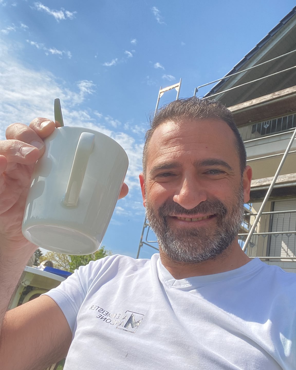 Pietro Manzone lächelt mit einer Tasse Kaffee vor einer Baustelle